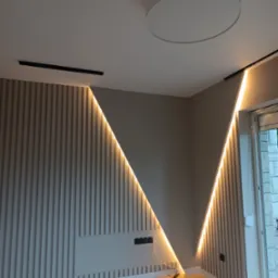 Nowoczesny salon z dekoracyjną ścianą z pionowych paneli, podświetlonych ledami w kształcie litery V, okrągła lampa sufitowa i szynoprzewód oświetleniowy