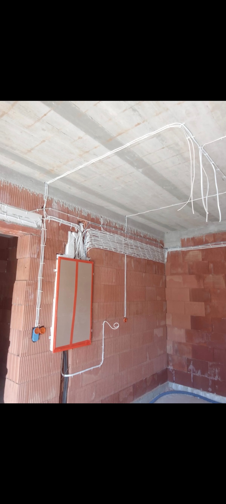 Rozprowadzone przewody elektryczne po suficie i ścianach w surowym wnętrzu z czerwonej cegły, widoczna skrzynka rozdzielcza z zabezpieczeniem na ścianie.