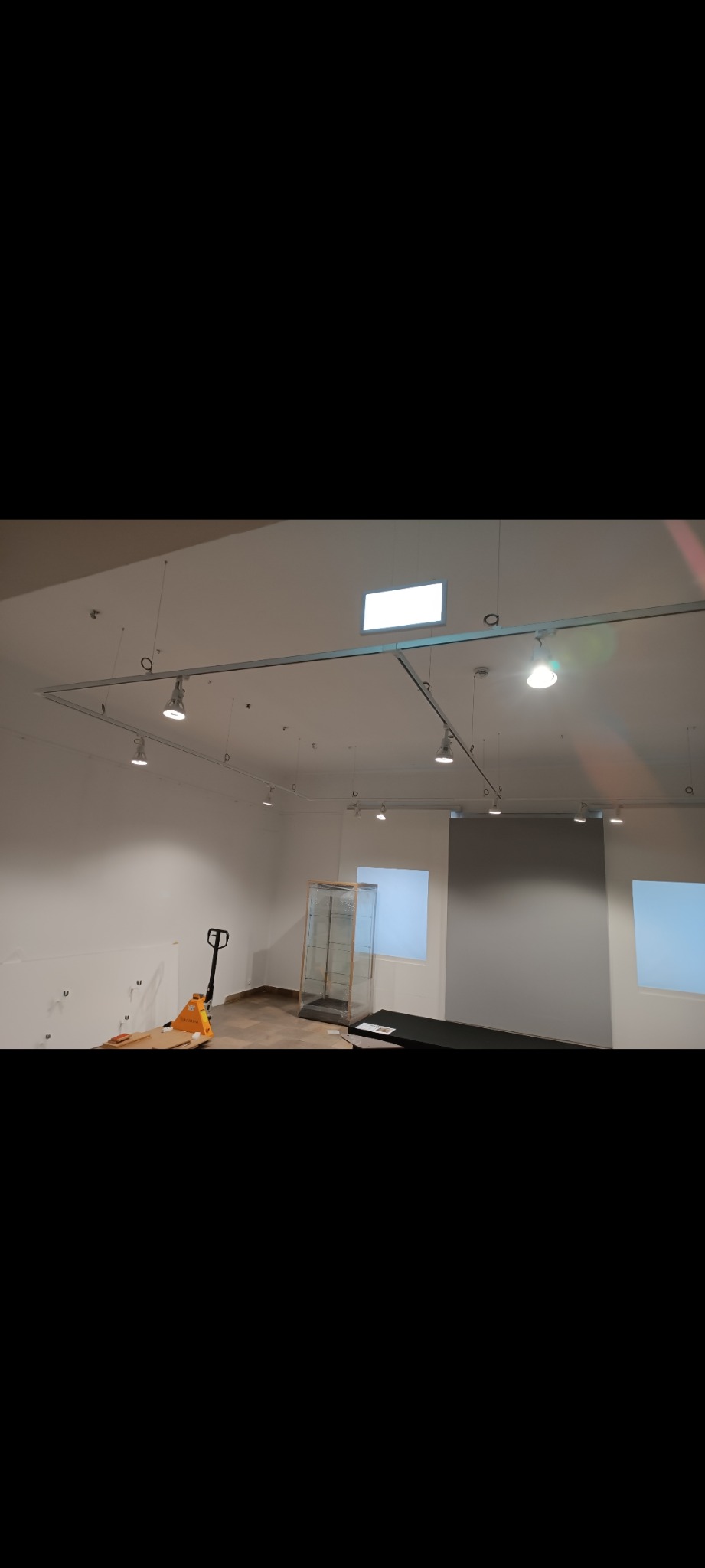 Wnętrze sklepu w trakcie przygotowań do otwarcia, widoczne szyny oświetleniowe pod sufitem, paleciak i gablota wystawowa