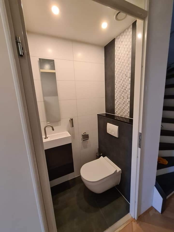 Nowoczesna, mała łazienka z wiszącą toaletą, umywalką nablatową na szafce w kolorze ciemnego drewna, biało-szarą mozaiką na ścianie i podświetleniem punktowym.