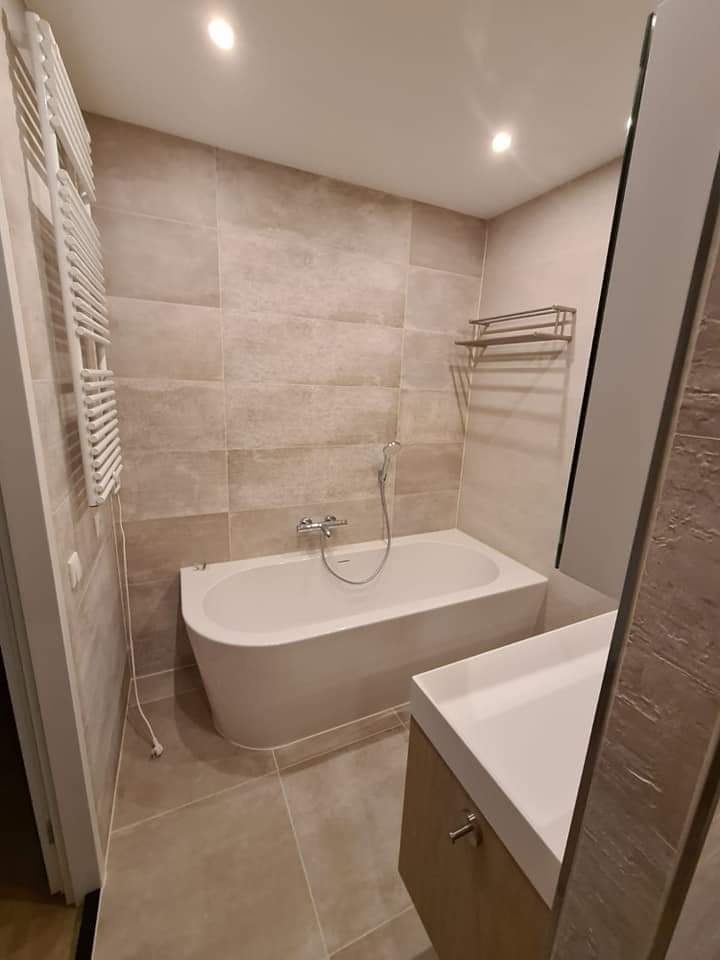 Nowoczesna łazienka w beżowych odcieniach z wolnostojącą wanną, umywalką nablatową i grzejnikiem drabinkowym.