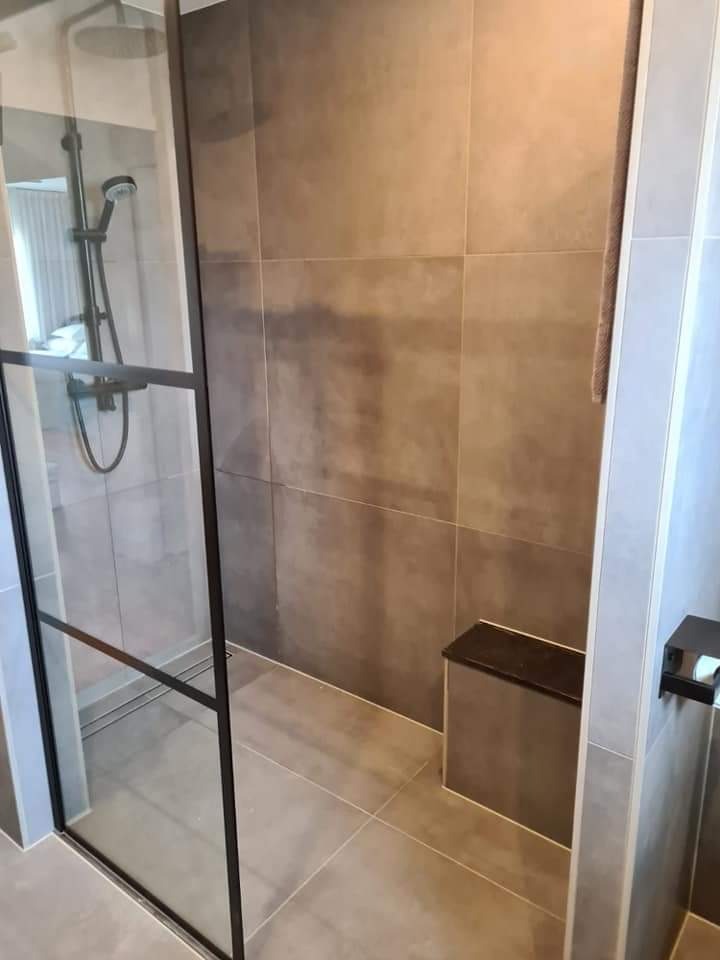 Nowoczesna kabina prysznicowa z czarnymi profilami, szare płytki imitujące beton, wbudowane siedzisko i deszczownica.