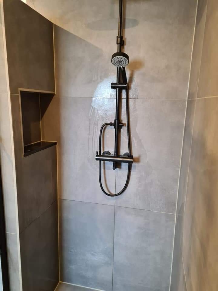 Szara łazienka z kabiną prysznicową i czarną armaturą, wnęka w ścianie wykończona płytkami.