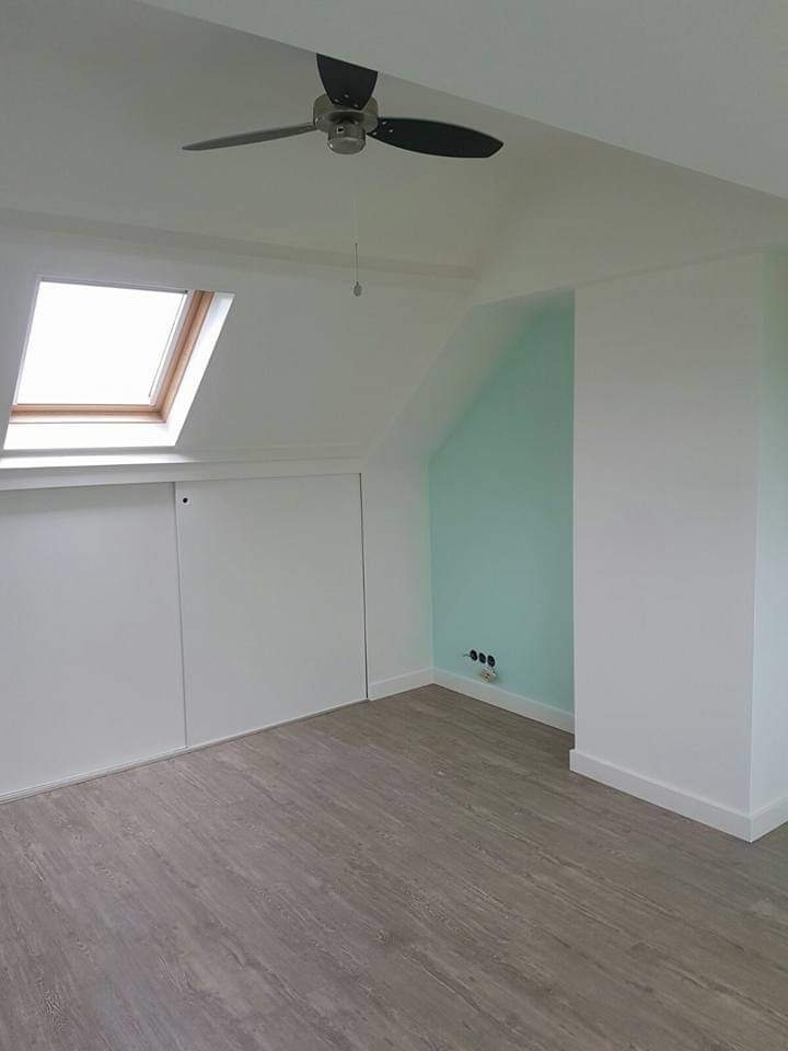 Poddasze po remoncie: białe ściany, szara podłoga, okno dachowe, wbudowana szafa z przesuwnymi drzwiami i fragment ściany pomalowany na miętowo z widocznymi gniazdkami elektrycznymi.