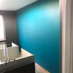 Świeżo pomalowane biuro z turkusową ścianą, szarą ścianą przy oknie i fragmentem białych biurek.