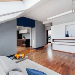 Jasne wnętrze mieszkania na poddaszu z szarą tapetą w poziome paski, drewnianą podłogą i otwartą kuchnią w tle.