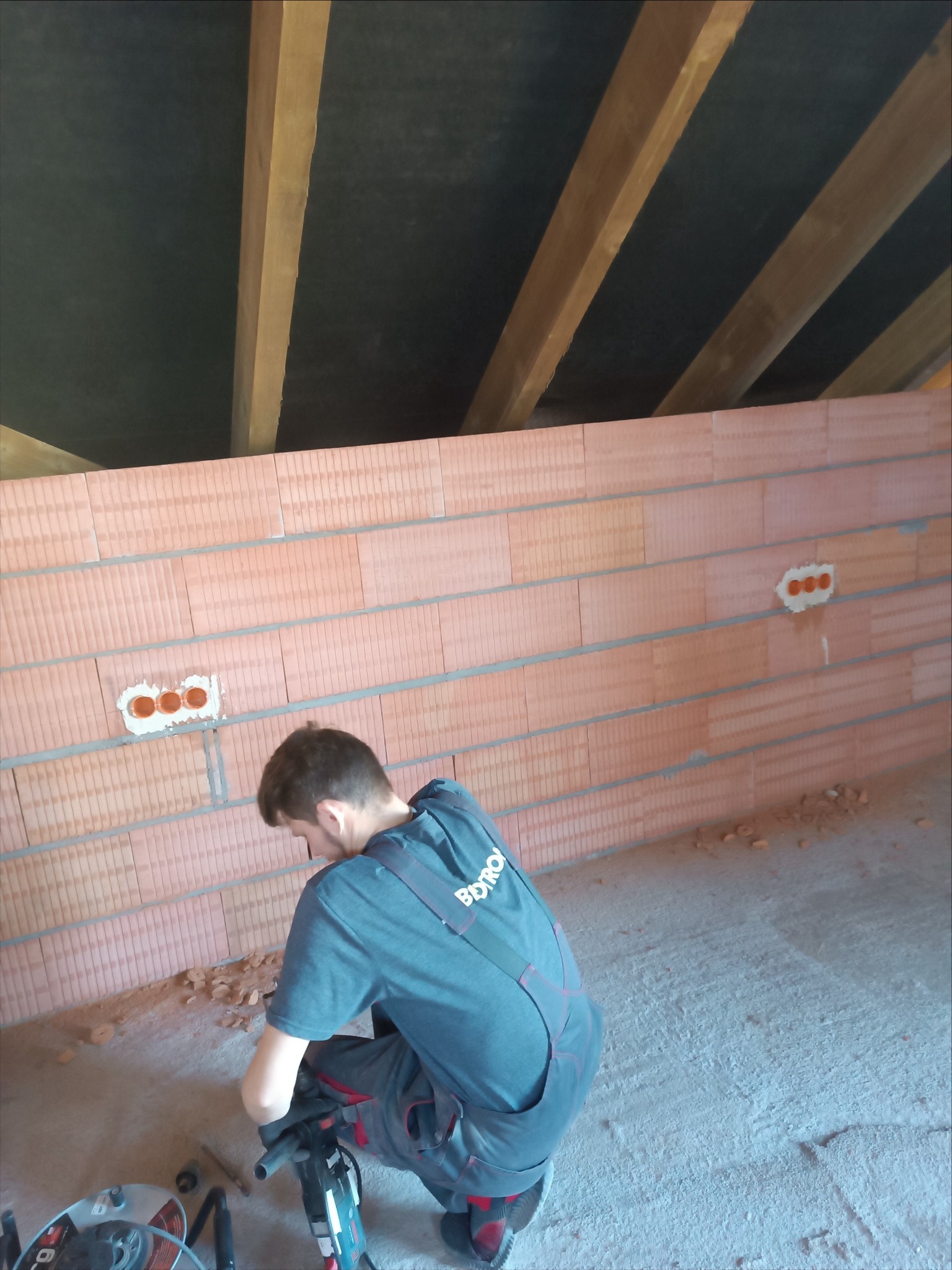 Elektryk w trakcie bruzdowania ściany pod instalację elektryczną w nowym budynku. Widoczne puszki pod gniazdka i narzędzia pracy.