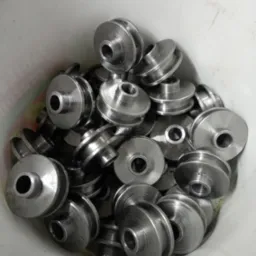 Partia obrobionych, metalowych kół pasowych w plastikowym pojemniku, widoczne ślady obróbki skrawaniem.