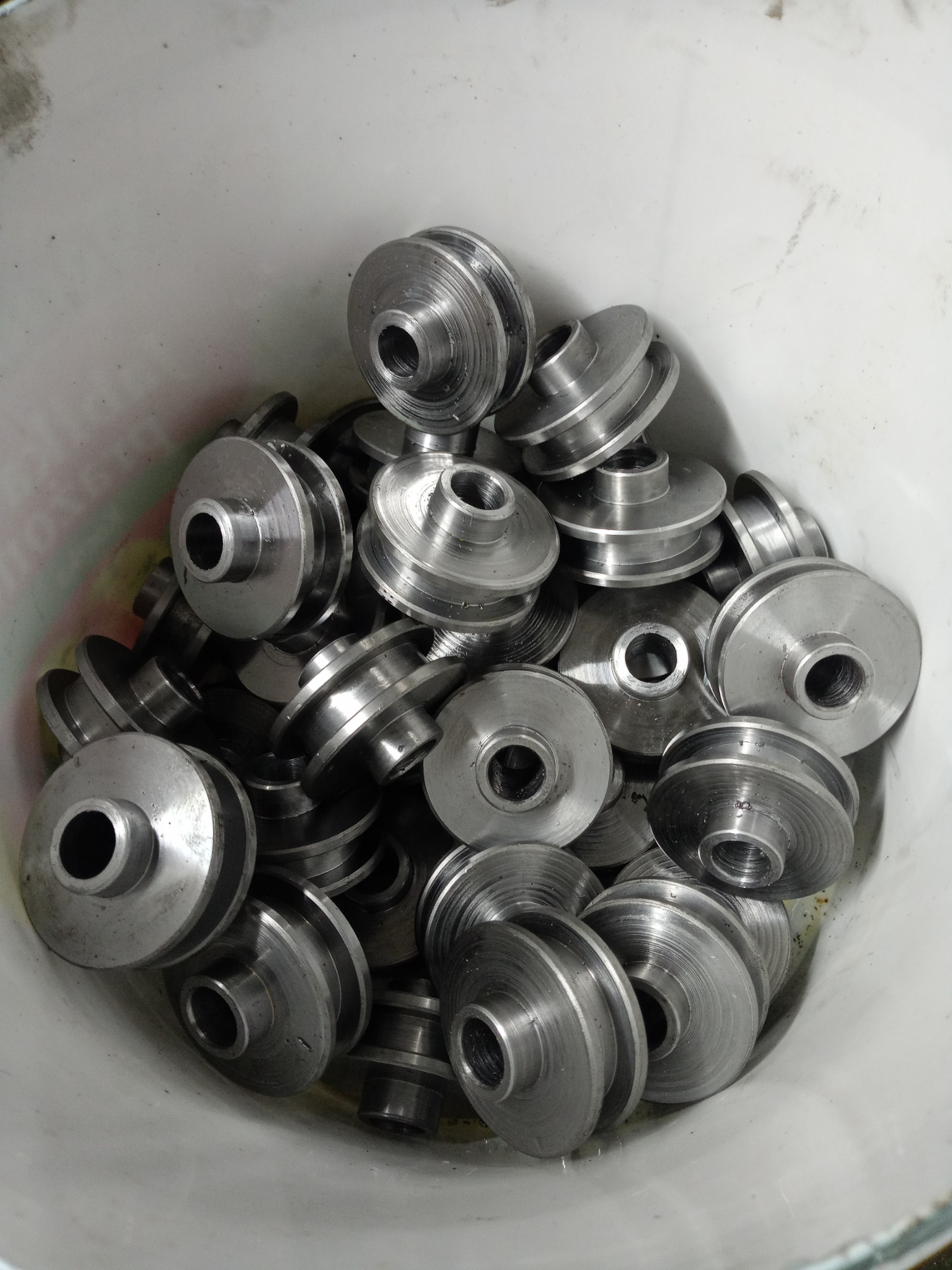 Partia obrobionych, metalowych kół pasowych w plastikowym pojemniku, widoczne ślady obróbki skrawaniem.