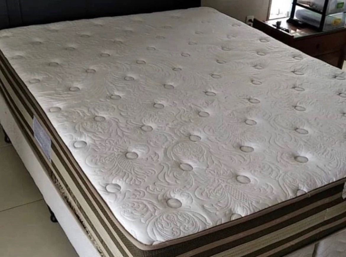 Materac z kremową tapicerką w kwiatowe wzory i guzikami, widoczny fragment ramy łóżka i stolika nocnego w tle.