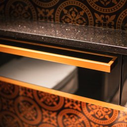 GLASS DECORATOR SPÓŁKA Z OGRANICZONĄ ODPOWIEDZIALNOŚCIĄ - Szklana balustrada z czarnym blatem i złotymi zdobieniami, widoczny fragment umywalki