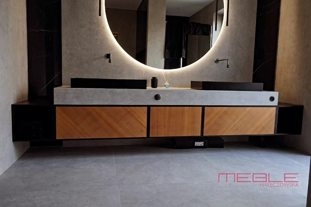 Nowoczesna łazienka z podwójną umywalką nablatową, okrągłym lustrem z podświetleniem LED i drewnianymi frontami szafek z ukośnym wzorem.