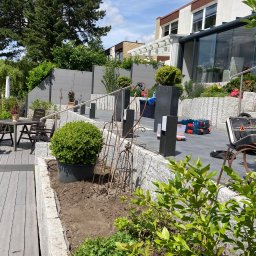 BS BudSerwis - Nowoczesny taras z drewnianą podłogą i kamiennymi elementami, uzupełniony o roślinność i meble ogrodowe. Widoczne narzędzia sugerują prace wykończeniowe.