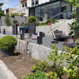 BS BudSerwis - Granitowe schody i taras z narzędziami w Olsztynie. W tle nowoczesny dom z przeszkloną werandą i rośliny w donicach. Prace wykończeniowe w ogrodzie.