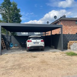 BS BudSerwis - Nowoczesna wiata garażowa w kolorze antracytowym, z zaparkowanym białym samochodem. W tle dom z cegły i fragment ogrodzenia panelowego.