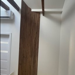 BS BudSerwis - Nowoczesna aranżacja wnętrza: drewniane lamele na ścianie, białe ściany, klimatyzator i widoczne fragmenty drewnianych belek sufitowych, tworząca unikalny design.