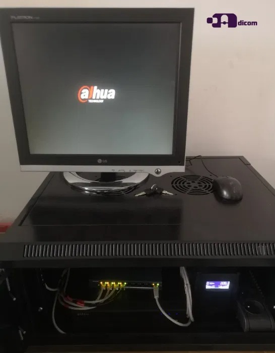 Monitor z logo Dahua na szafie rack z przełącznikiem sieciowym, myszką i kluczem na górze