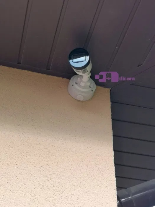 Kamera monitoringu typu bullet zamontowana na elewacji budynku pod drewnianym podbitką dachową.