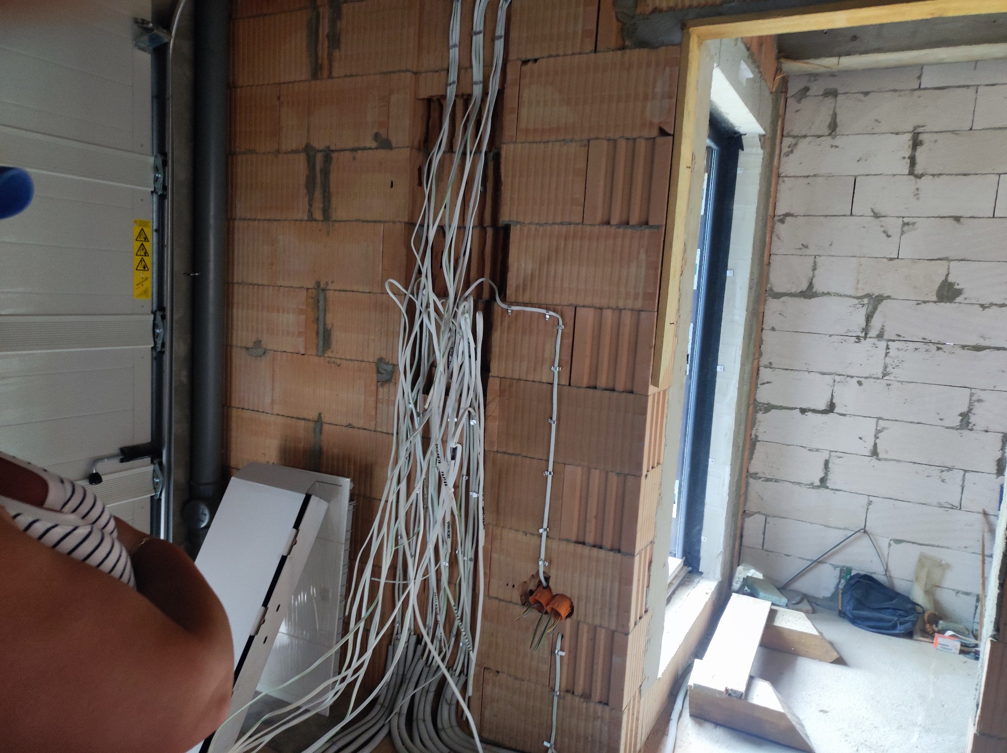 Nowe okablowanie elektryczne w surowym wnętrzu, widoczne przewody przytwierdzone do ściany z pustaków, instalacja w trakcie realizacji.