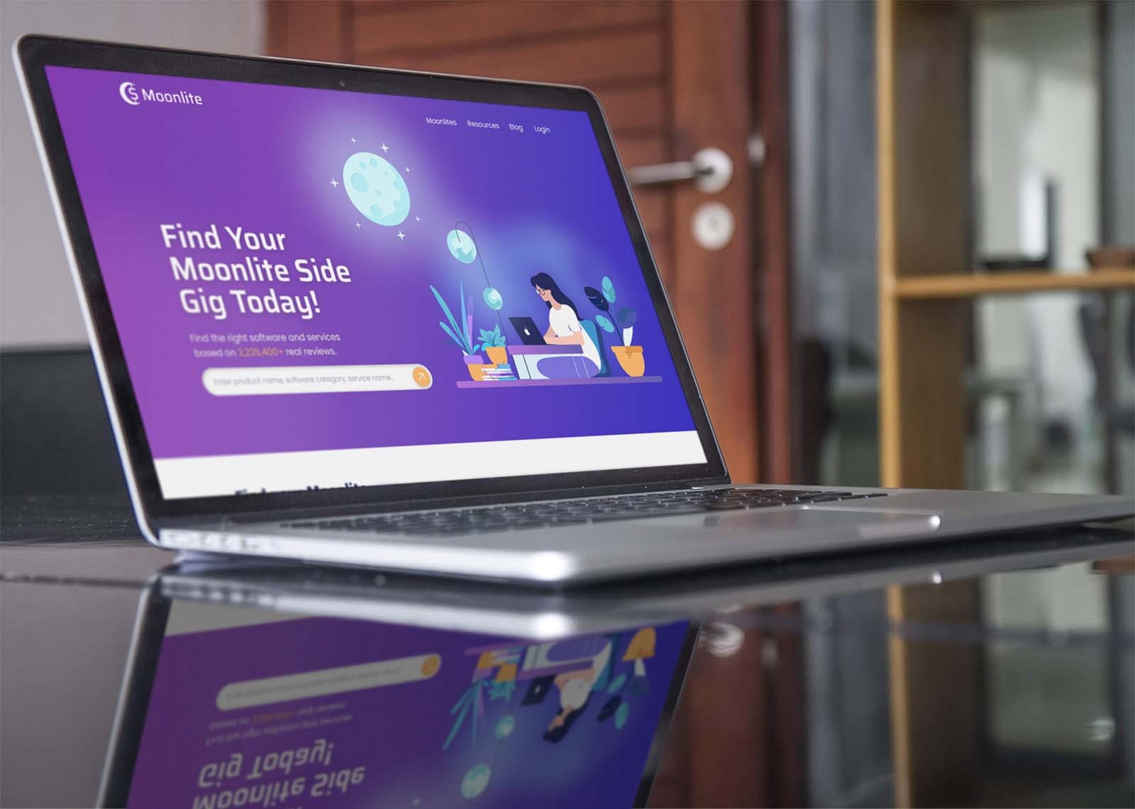 Laptop wyświetla stronę internetową Moonlite z ilustracją kobiety pracującej na laptopie, promującą znalezienie usług i oprogramowania, widoczne odbicie ekranu w błyszczącej powierzchni biurka.