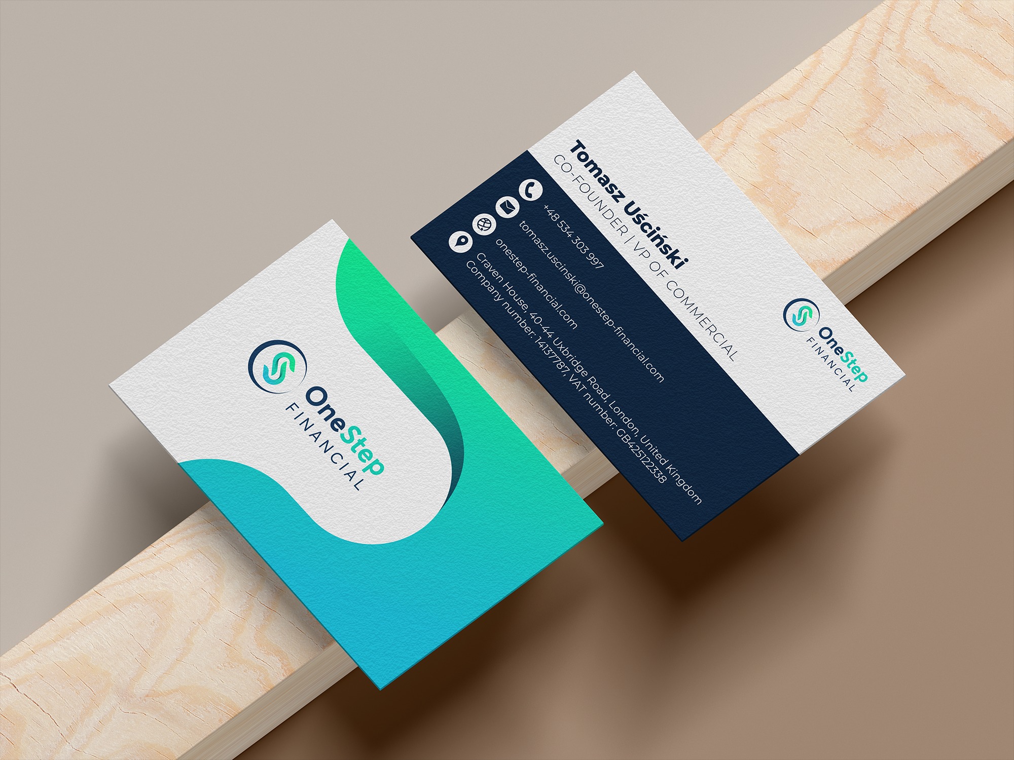 Dwie wizytówki firmy OneStep Financial leżące na drewnianym podłożu. Jedna z wizytówek ma granatowe tło z danymi kontaktowymi, druga białe tło z logo i gradientem w kolorach zieleni i błękitu.