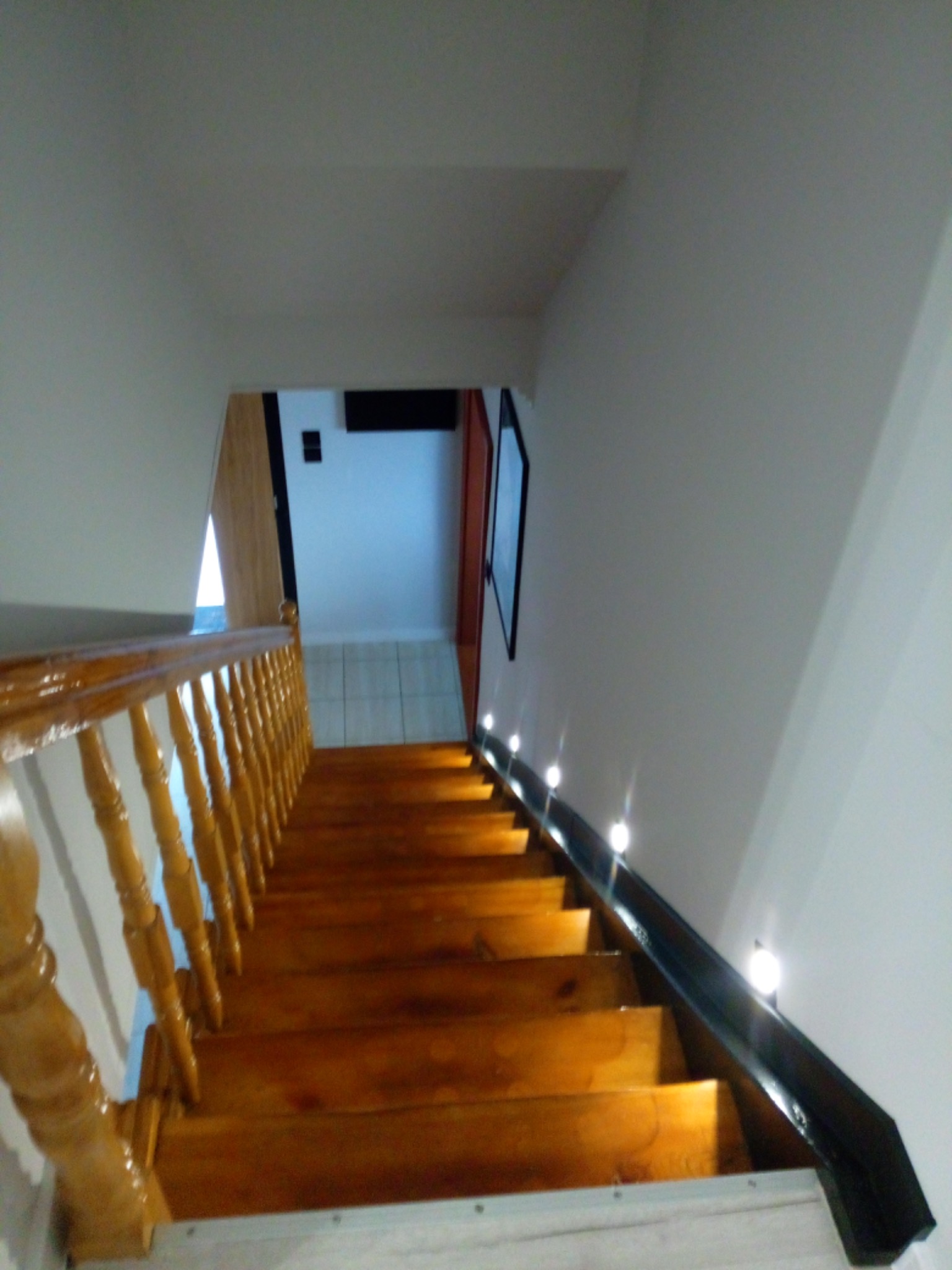 Drewniane schody z polakierowaną balustradą i oświetleniem punktowym wzdłuż ściany.