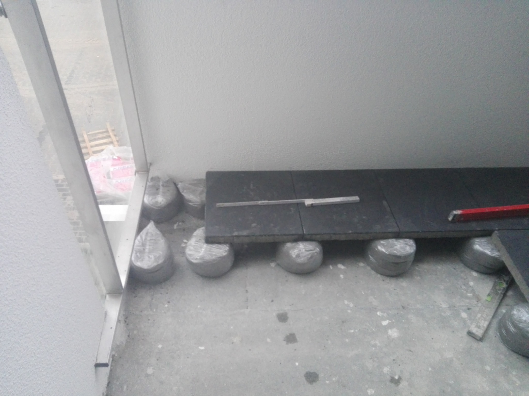 Montaż płytek na balkonie z użyciem regulowanych wsporników, widoczny poziomica i zapas płytek w folii.