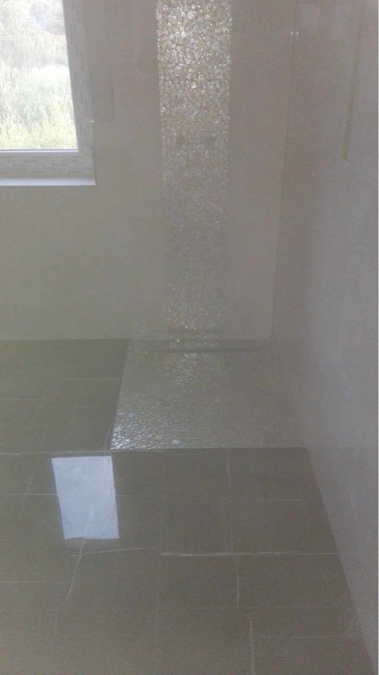 Wykończona łazienka z ciemnymi płytkami podłogowymi i dekoracyjnym panelem ściennym z mozaiki szklanej, widok na okno z zielenią na zewnątrz.