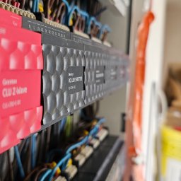 CleverHouse Paweł Piotrowski - Panel sterowania inteligentnego domu Grenton z modułami CLU Z-Wave i ROLLER SHUTTER, widoczne przewody i elementy instalacji, w tle kartony i wiadro.