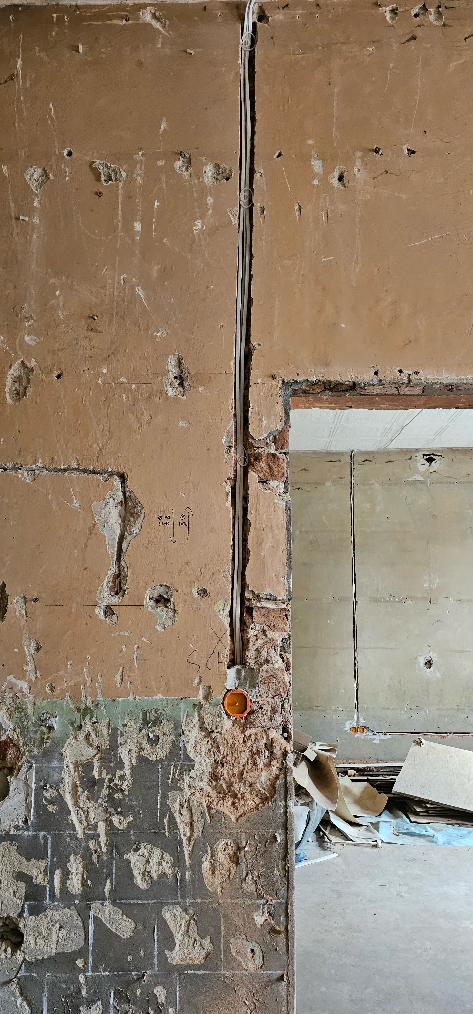 Wnętrze w trakcie remontu: widoczne kable elektryczne prowadzone po ścianie z uszkodzonym tynkiem, puszka instalacyjna i fragment muru z cegły. Widoczne ślady po kuciu.