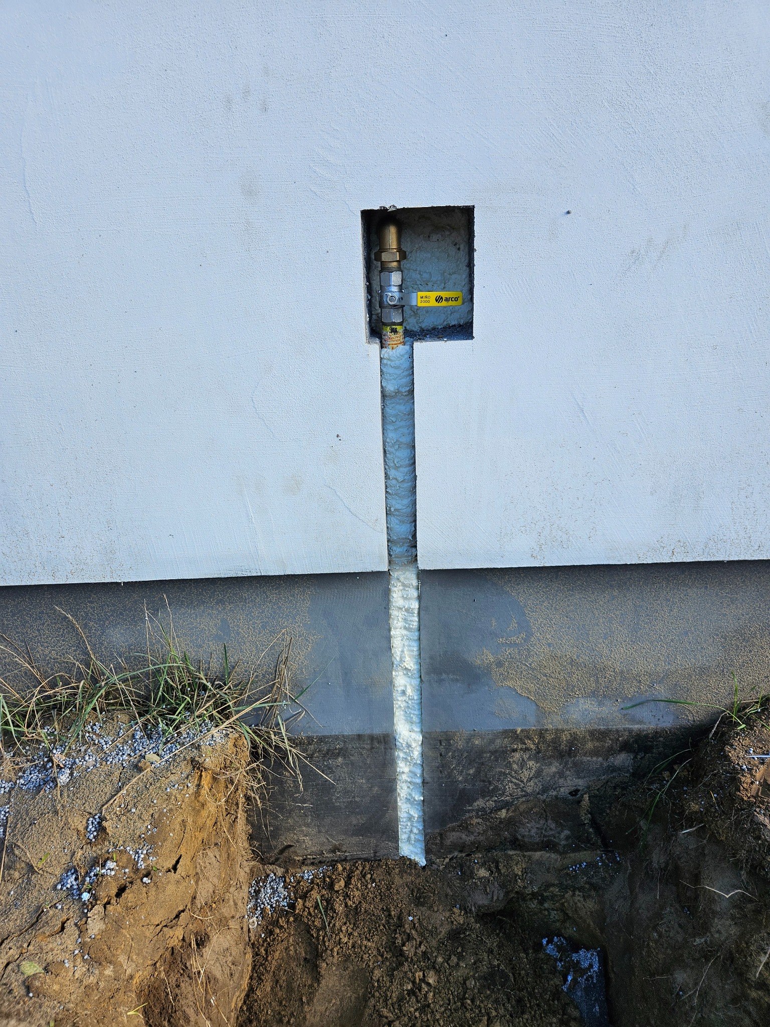 Świeżo wykonane przyłącze gazowe do budynku, widoczna rura gazowa zabezpieczona pianką montażową w wykopie, z zaworem ARCO Micro 2000 w ścianie.