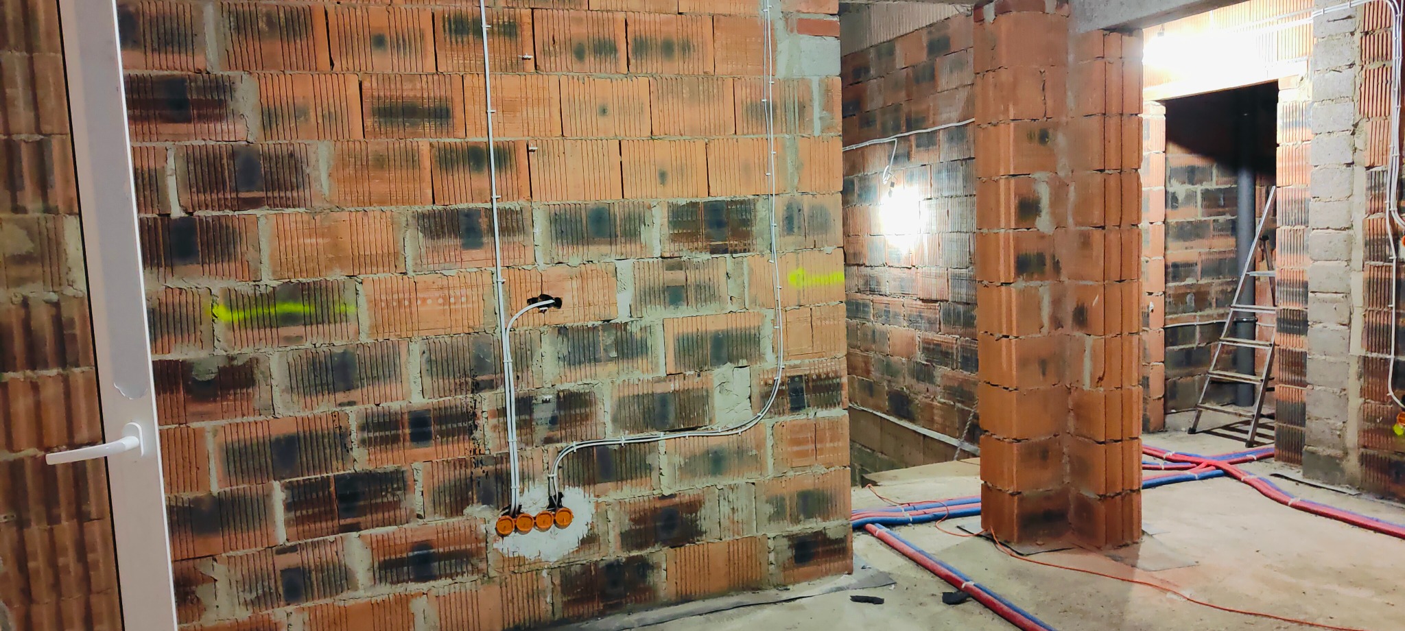 Wnętrze w trakcie prac wykończeniowych: ściany z czerwonej cegły dziurawki z widocznymi przewodami elektrycznymi w białych rurkach, puszki pod gniazdka i włączniki w przygotowanych otworach,...