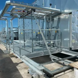 Instalacja przemysłowa na dachu z metalową konstrukcją wsporczą, widoczne rury izolowane termicznie i elementy wentylacyjne.