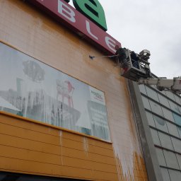 Grzegorz Gańczak - Pracownik na podnośniku czyści elewację budynku handlowego z reklamą Agata Meble. Widoczne zacieki po myciu i narzędzie do czyszczenia na długim kiju.