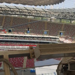 Grzegorz Gańczak - Widok z góry na stadion z elementami konstrukcyjnymi i sprzętem. W tle widoczne trybuny i zadaszenie stadionu. Ujęcie z dużej wysokości.