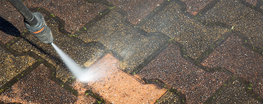 Dysza myjki ciśnieniowej czyści kostkę brukową, usuwając zabrudzenia. Widoczna różnica w kolorze między czystą a brudną powierzchnią. Ujęcie z góry, skupione na detalu.