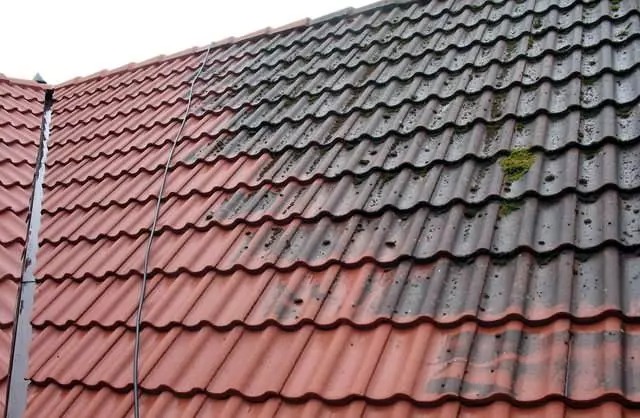 Częściowo wyczyszczony dach z czerwonej dachówki, widoczna różnica między czystą a zabrudzoną powierzchnią. Mech na brudnej części. Ujęcie z góry.