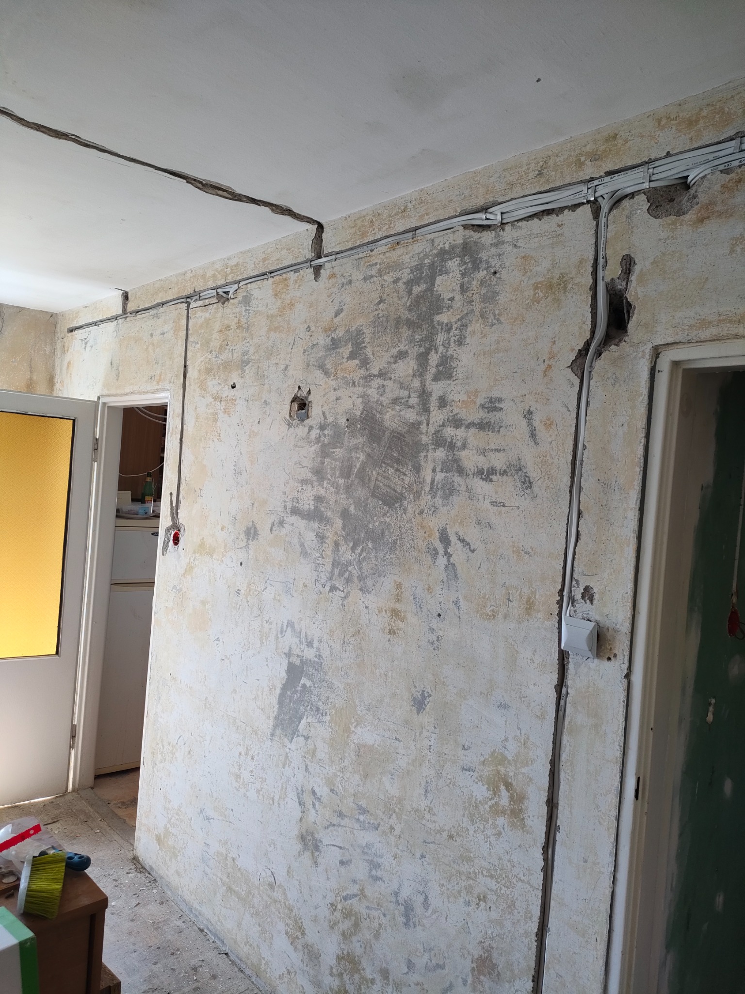 Ściana w trakcie przygotowania do prac wykończeniowych, widoczne ślady po starych powłokach, instalacje elektryczne w listwach, szczelina w suficie.