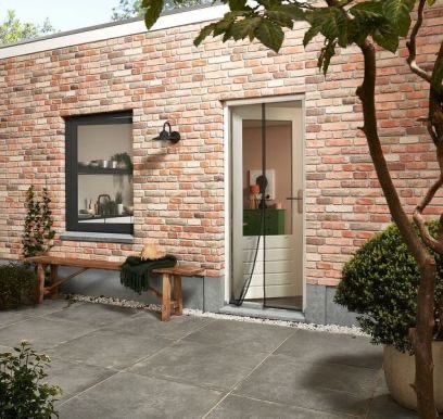Zewnętrzny widok na dom z zamontowaną siatką magnetyczną w drzwiach wejściowych, na tle ceglanej ściany i drewnianej ławki.