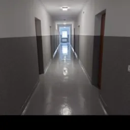 Długi korytarz po remoncie z szarą, teksturowaną dolną częścią ścian i białą górną, świeżo pomalowany na szaro błyszczący parkiet, drzwi po obu stronach korytarza.