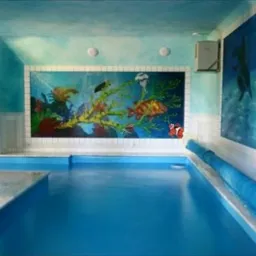 Kryty basen z mozaiką przedstawiającą podwodny świat i muralem z delfinami, zabezpieczony niebieską roletą, w rezydencji w Karpaczu.