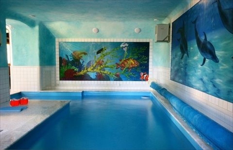 Kryty basen z mozaiką przedstawiającą podwodny świat i muralem z delfinami, zabezpieczony niebieską roletą, w rezydencji w Karpaczu.