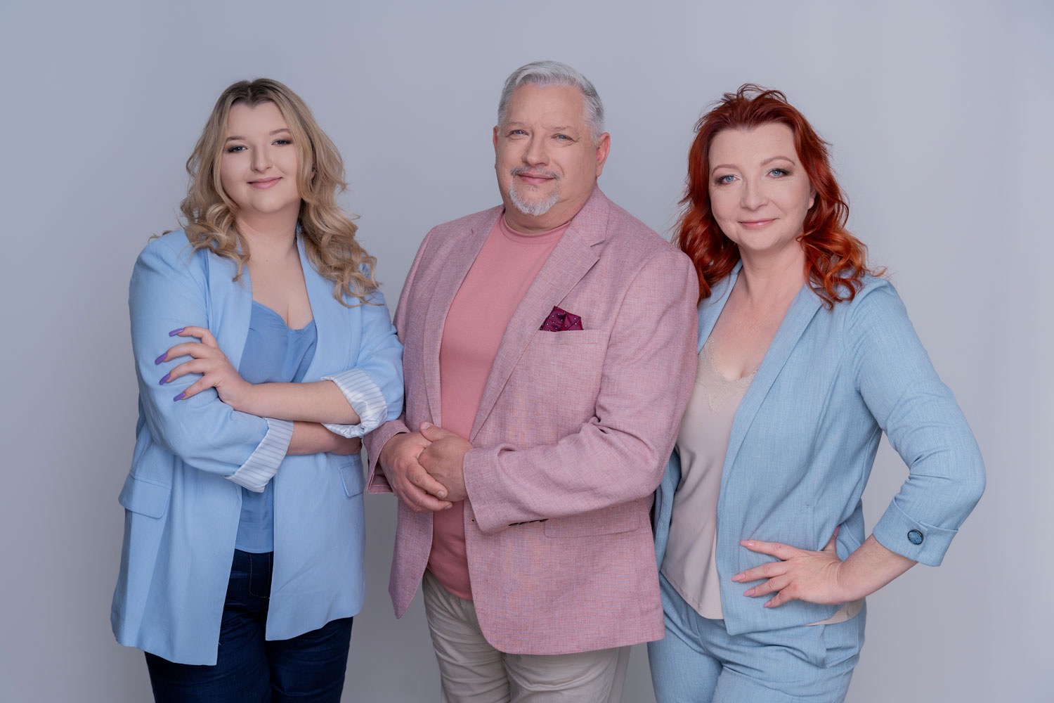 Portret grupowy: młoda blondynka, mężczyzna z siwą brodą i kobieta z rudymi włosami, wszyscy w pastelowych marynarkach, na jasnym tle. Zespół biura rachunkowego.
