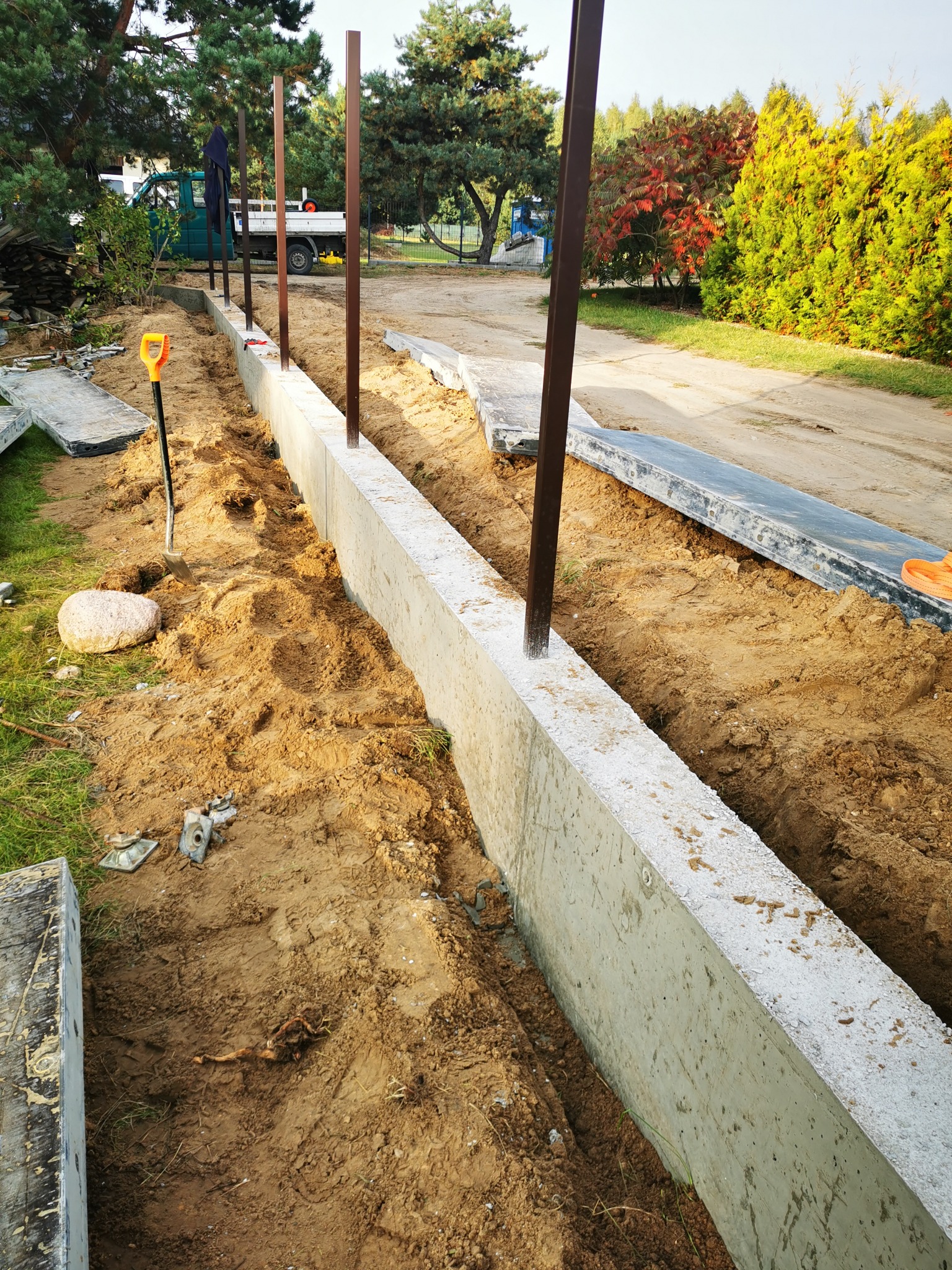 Fundament betonowy pod ogrodzenie z metalowymi słupkami w trakcie montażu w Warszawie, widoczna ziemia i narzędzia.