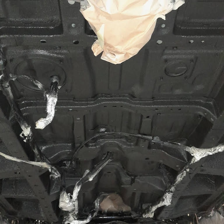 Podwozie samochodu po nałożeniu czarnej powłoki ochronnej, zabezpieczone taśmą elementy przed malowaniem.