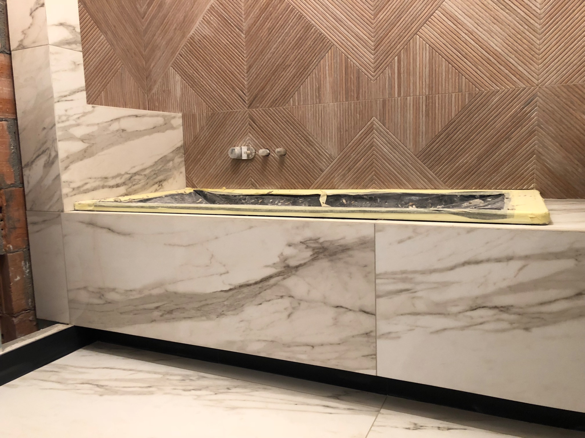 Przygotowanie do montażu umywalki w łazience z marmurową zabudową i dekoracyjną ścianą z drewnopodobnych płytek o wzorze chevron.