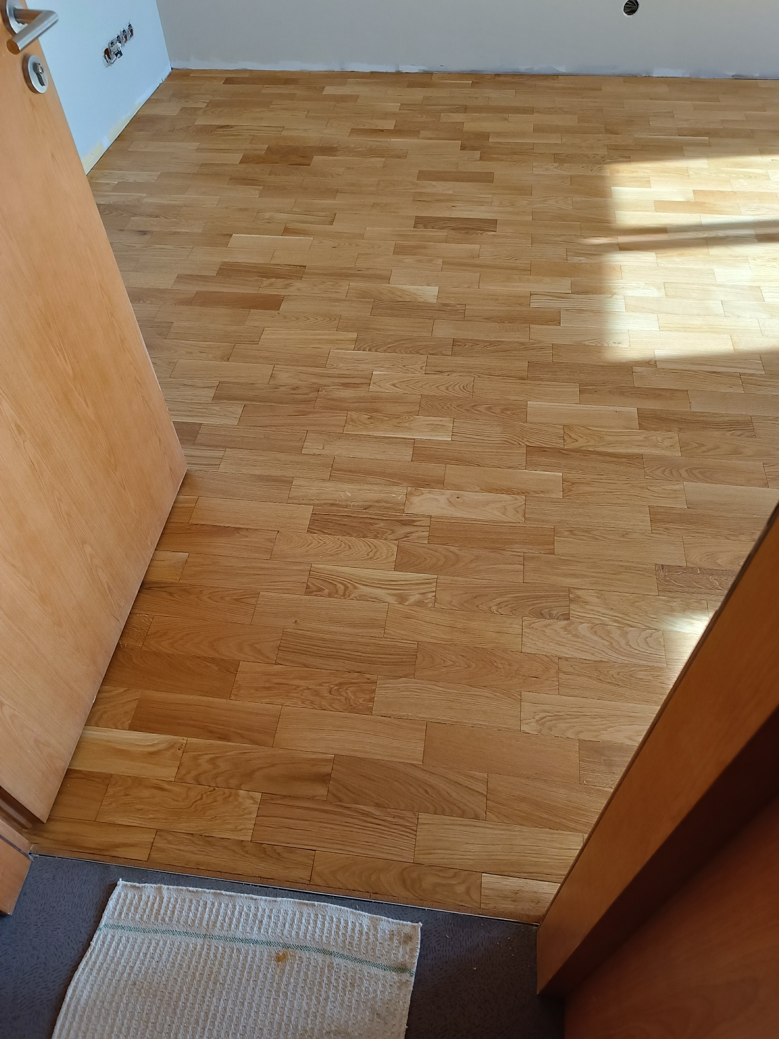 Ułożony parkiet w Gdańsku, widok zza otwartych drzwi, na podłodze leży mała wycieraczka.