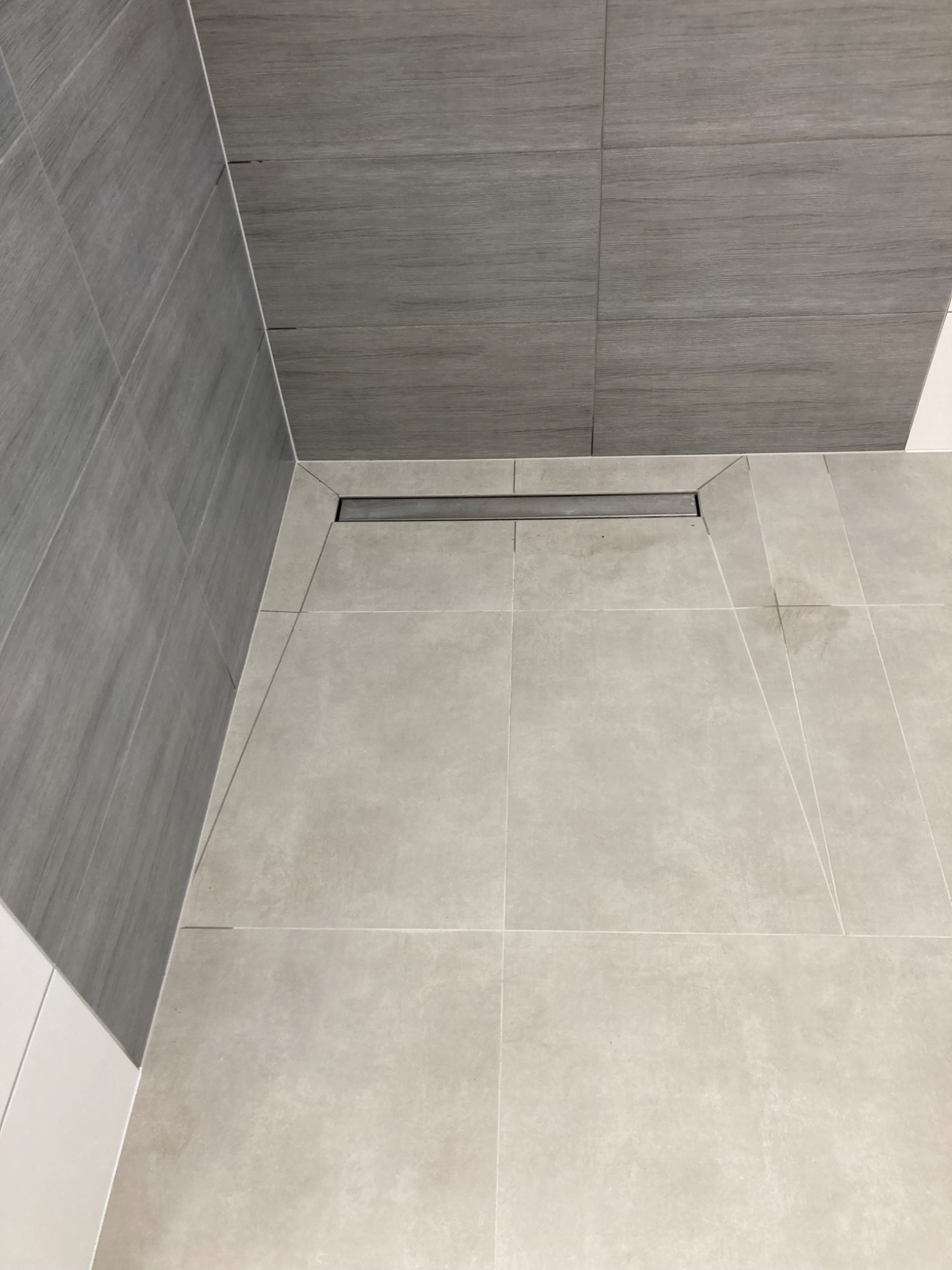 Wykończona łazienka z szarymi płytkami imitującymi drewno na ścianach i jasnoszarą podłogą z odpływem liniowym.