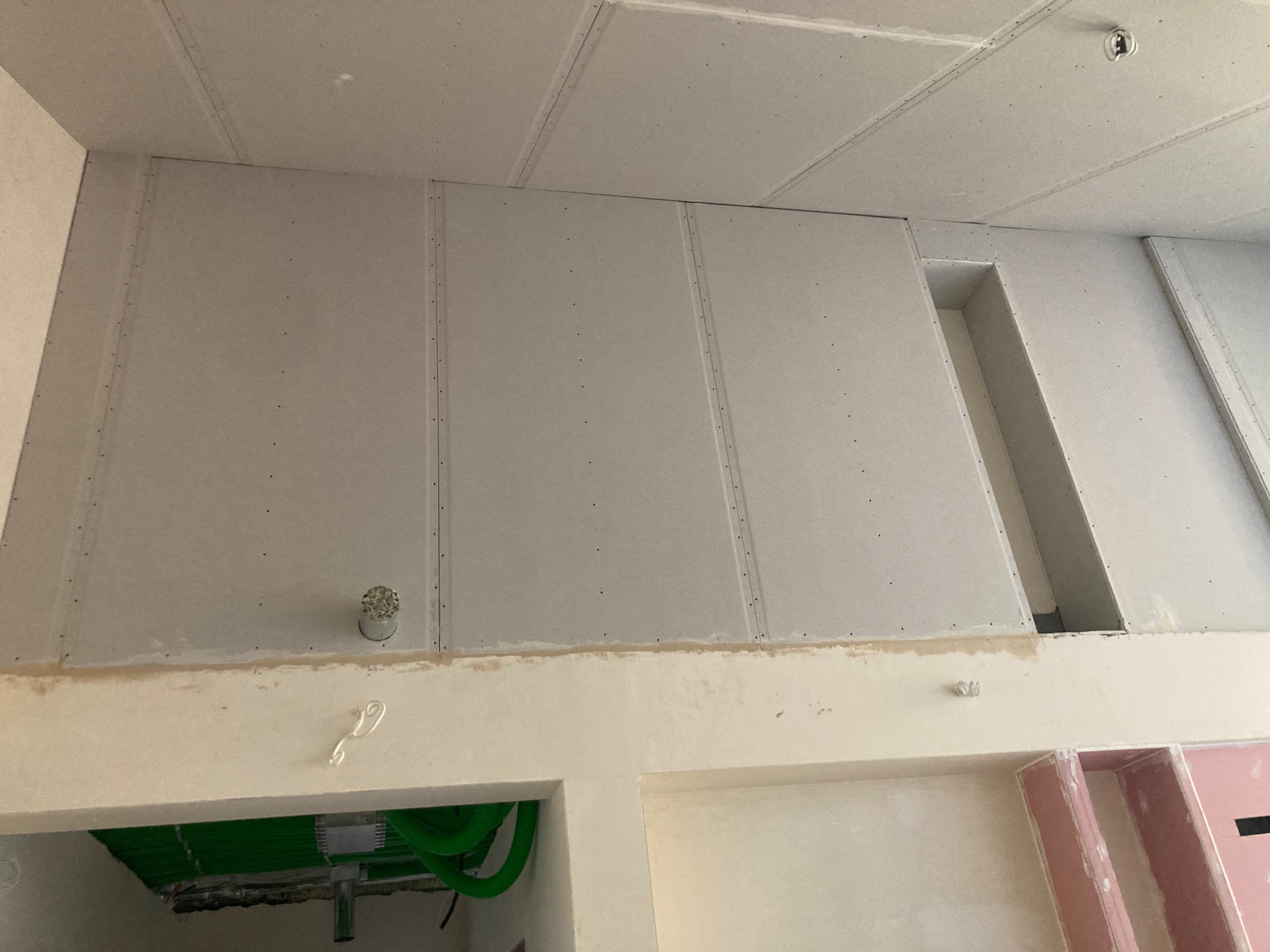 Montaż płyt gipsowo-kartonowych na ścianie i suficie, widoczne łączenia i otwory wentylacyjne, instalacja elektryczna w tle.