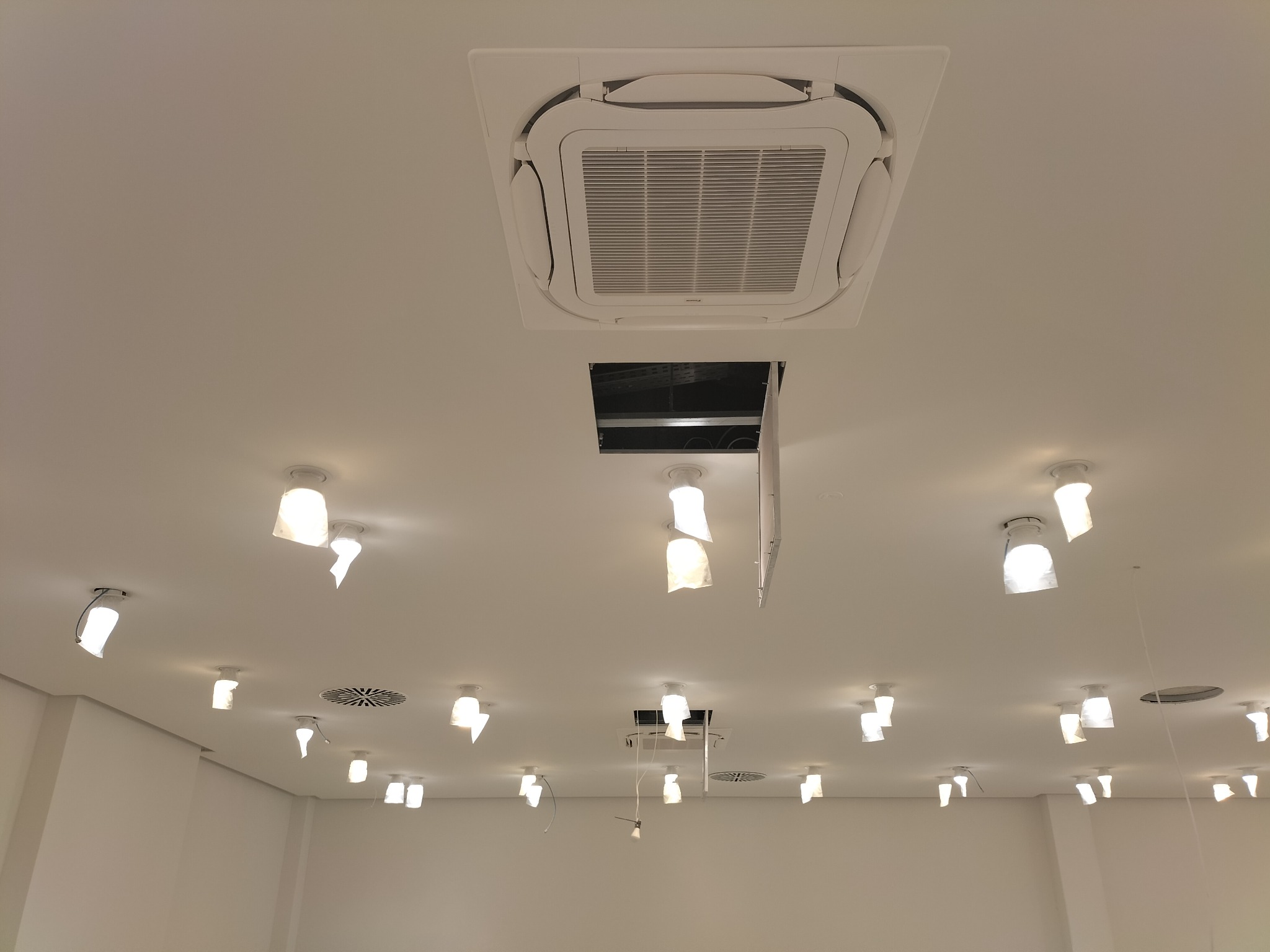 Sufit w biurze w Krakowie z zamontowaną kasetonową jednostką klimatyzacyjną i otwartym panelem dostępowym, otoczony licznymi lampami o nietypowych kloszach.